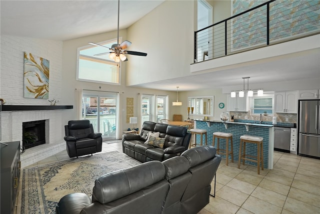 living room featuring a brick fireplace, a towering ceiling, ceiling fan, and light tile patterned flooring