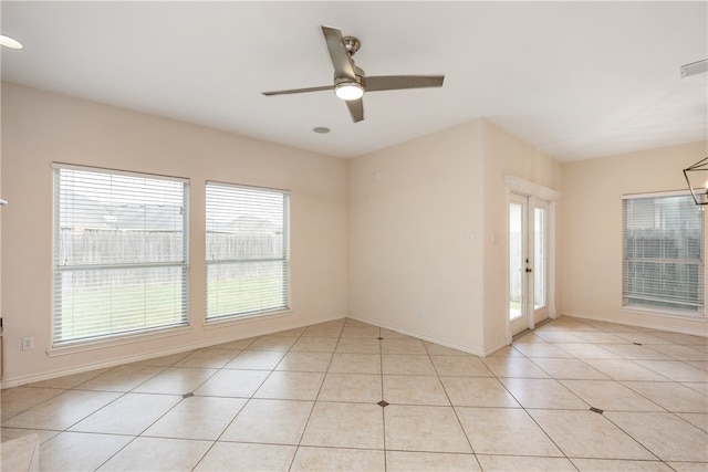 tiled spare room featuring a wealth of natural light and ceiling fan with notable chandelier