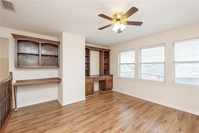 unfurnished living room featuring light wood-type flooring, built in desk, and ceiling fan