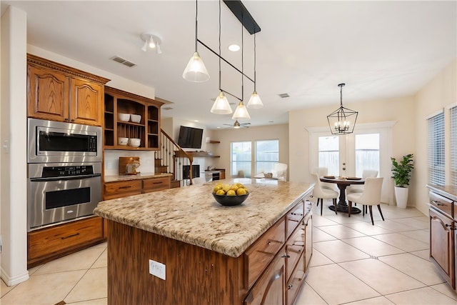 kitchen featuring a kitchen island, light tile patterned floors, pendant lighting, light stone countertops, and ceiling fan with notable chandelier