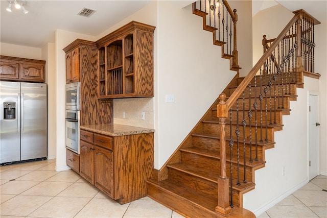 kitchen with backsplash, light stone counters, light tile patterned floors, and stainless steel appliances