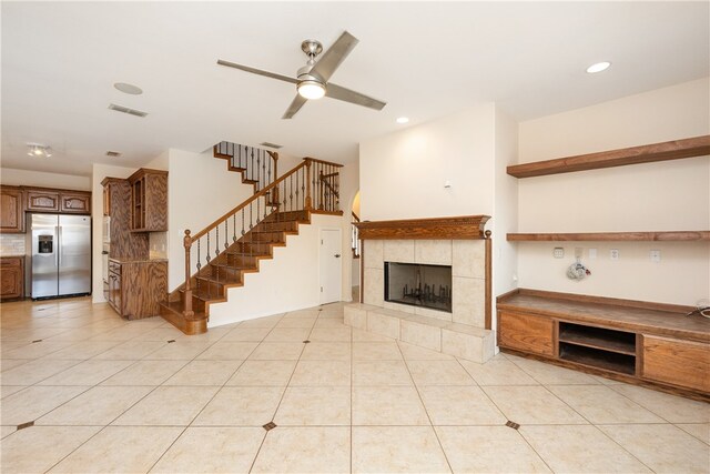 unfurnished living room featuring ceiling fan, a tile fireplace, and light tile patterned flooring