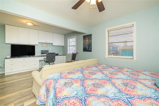 bedroom featuring built in desk, ceiling fan, and light hardwood / wood-style flooring