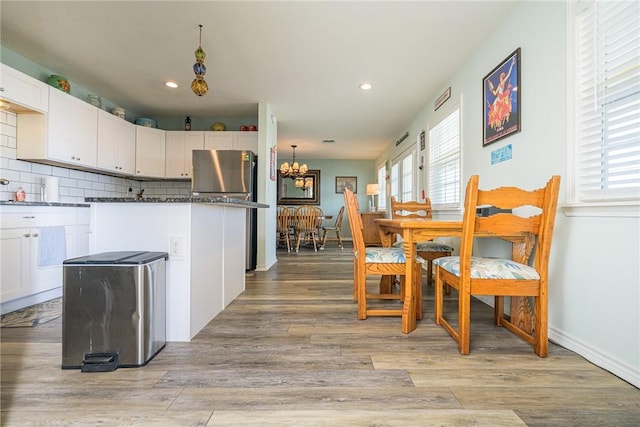 kitchen featuring a chandelier, stainless steel fridge, light hardwood / wood-style floors, decorative backsplash, and white cabinets