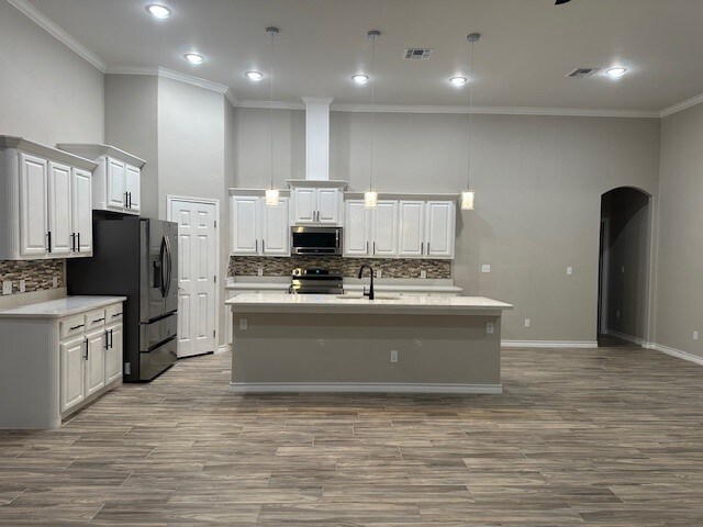 kitchen featuring stainless steel appliances, a kitchen island with sink, crown molding, decorative light fixtures, and white cabinets