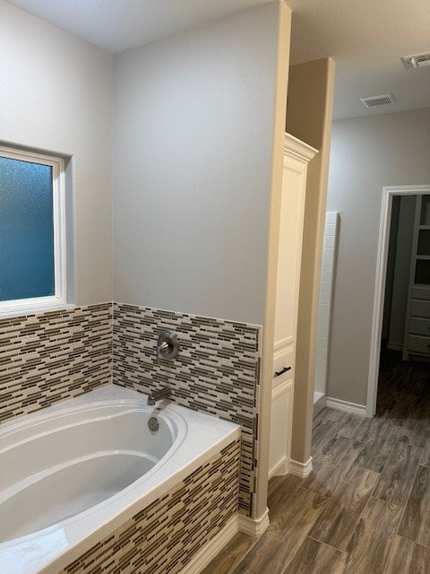 bathroom featuring hardwood / wood-style floors and a relaxing tiled tub