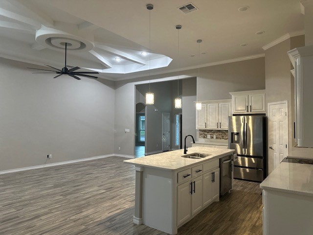 kitchen featuring a kitchen island with sink, sink, appliances with stainless steel finishes, decorative light fixtures, and white cabinetry