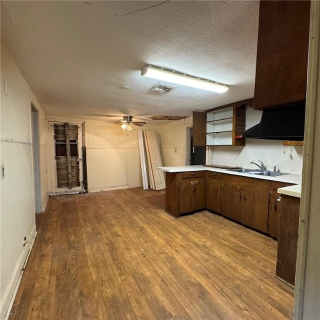 kitchen with kitchen peninsula, light wood-type flooring, a textured ceiling, dark brown cabinetry, and sink