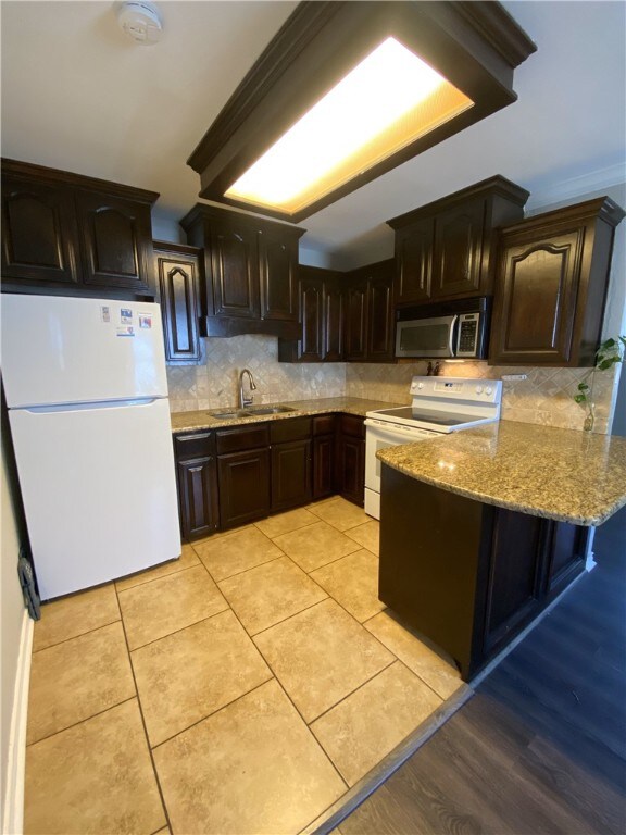 1038 Dorthy Dr, Corpus Christi, TX 78412 - kitchen with white appliances, light stone counters, a peninsula, decorative backsplash, and dark brown cabinetry