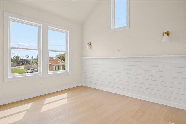 empty room featuring light wood finished floors, wooden walls, and lofted ceiling