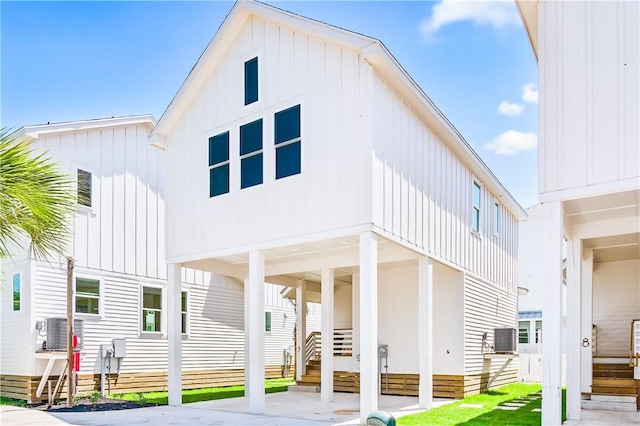 back of house with entry steps, a carport, central air condition unit, and board and batten siding