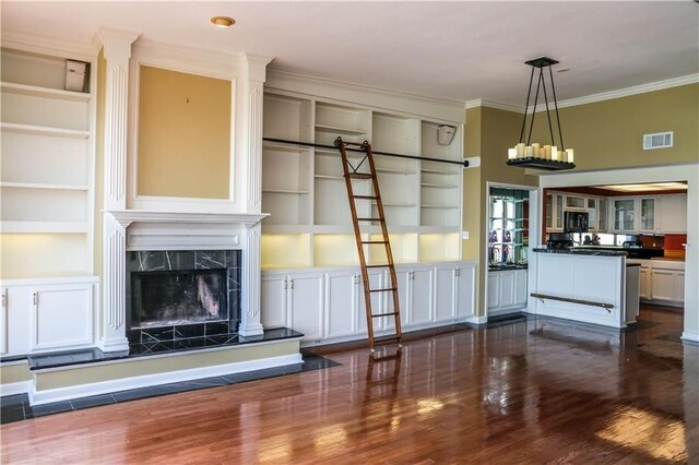 unfurnished living room with dark wood-type flooring, ornamental molding, a fireplace, and built in shelves