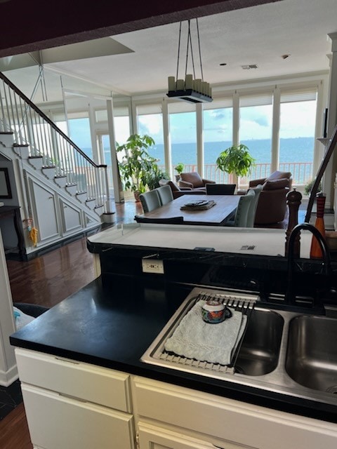 kitchen with sink, dark wood-type flooring, white cabinetry, hanging light fixtures, and a water view