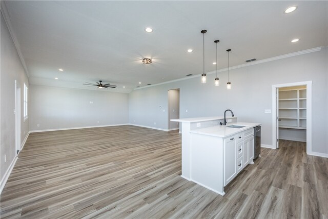 kitchen featuring sink, ornamental molding, hanging light fixtures, a kitchen island with sink, and light hardwood / wood-style flooring