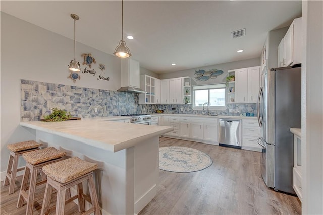 kitchen with appliances with stainless steel finishes, a peninsula, a sink, wall chimney range hood, and backsplash