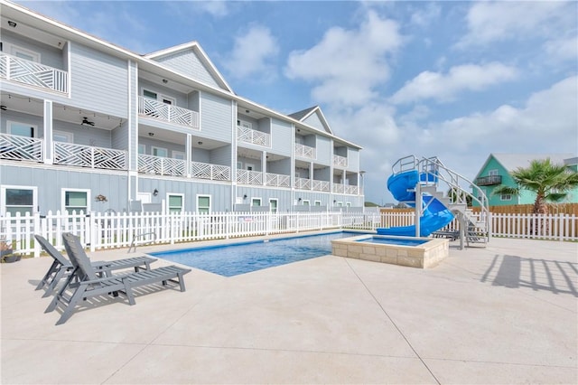 view of swimming pool featuring a patio, a water slide, fence, and a pool with connected hot tub