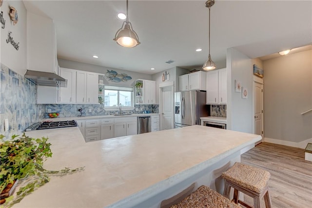 kitchen with stainless steel appliances, a peninsula, light countertops, wall chimney exhaust hood, and open shelves