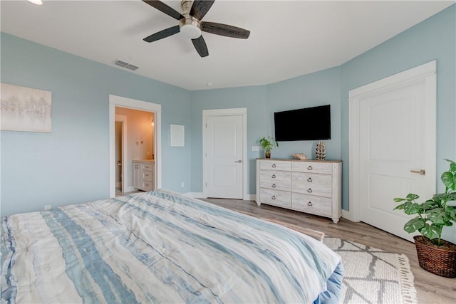 bedroom featuring visible vents, baseboards, a ceiling fan, ensuite bath, and wood finished floors