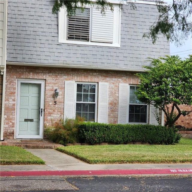 property entrance featuring a lawn, brick siding, and roof with shingles