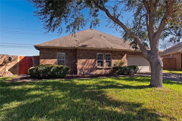 exterior space with an attached garage, brick siding, fence, roof with shingles, and a front lawn