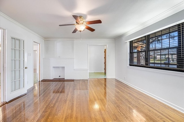 unfurnished living room featuring a large fireplace, wood finished floors, a ceiling fan, baseboards, and crown molding