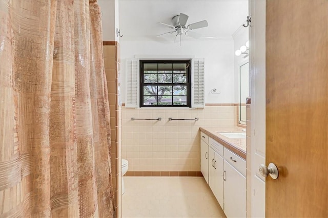 bathroom with toilet, a wainscoted wall, vanity, tile walls, and a ceiling fan