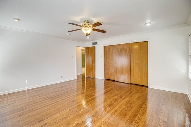 unfurnished bedroom featuring crown molding, light wood finished floors, a closet, visible vents, and baseboards