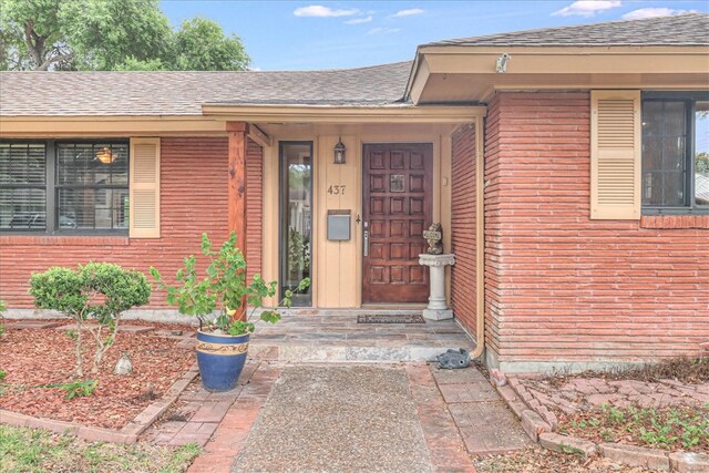 entrance to property featuring brick siding and roof with shingles