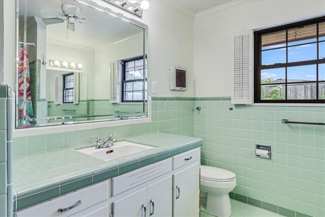 full bath with a ceiling fan, toilet, ornamental molding, vanity, and tile walls