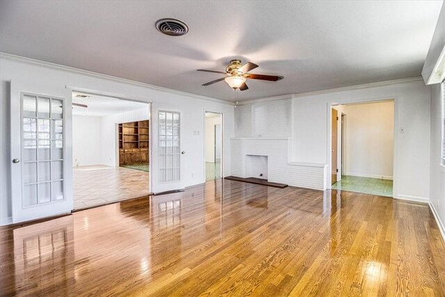 unfurnished living room with a brick fireplace, visible vents, wood finished floors, and ornamental molding