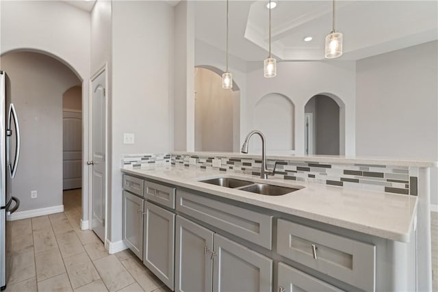 1706 Kentucky Derby Dr, Corpus Christi, TX 78417 - kitchen featuring gray cabinets, decorative backsplash, a sink, arched walkways, and light stone counters
