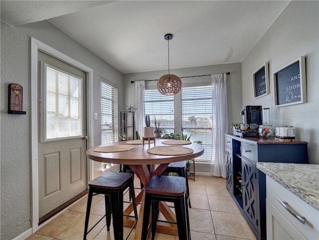 dining area featuring light tile patterned floors, a textured wall, and baseboards