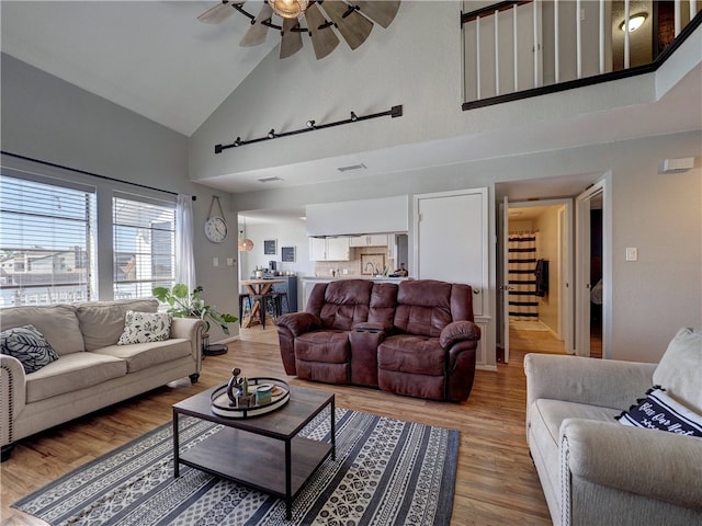 living area with stairway, light wood-style flooring, ceiling fan, high vaulted ceiling, and baseboards