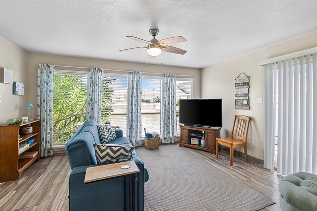 living room with a textured ceiling, ceiling fan, and light hardwood / wood-style flooring