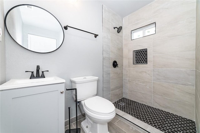 full bathroom with tiled shower, vanity, and toilet