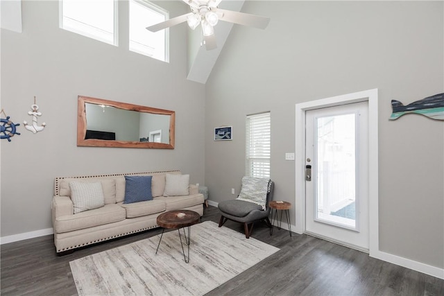 living room with a towering ceiling, a ceiling fan, baseboards, and wood finished floors