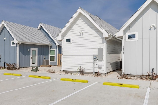 rear view of property featuring uncovered parking, board and batten siding, and roof with shingles