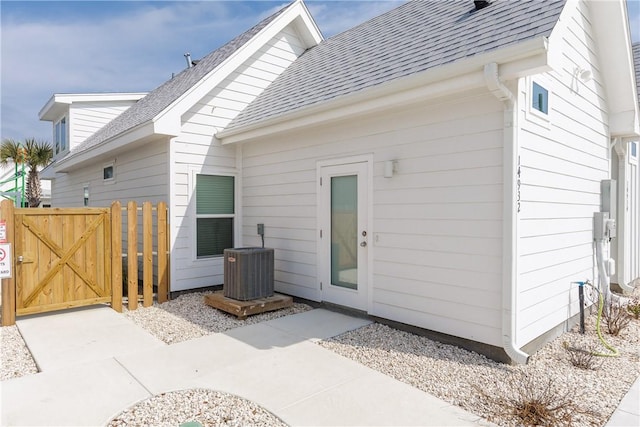 entrance to property with a shingled roof, cooling unit, a gate, and fence