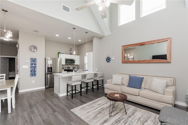 living area with a high ceiling, a ceiling fan, visible vents, baseboards, and dark wood finished floors