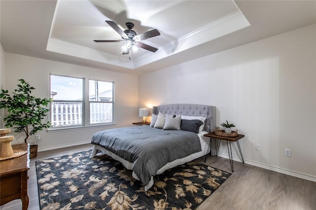 bedroom with a raised ceiling, ornamental molding, wood-type flooring, and ceiling fan