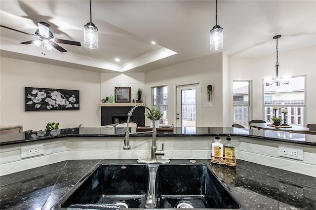 kitchen with dark stone counters, a raised ceiling, sink, and hanging light fixtures