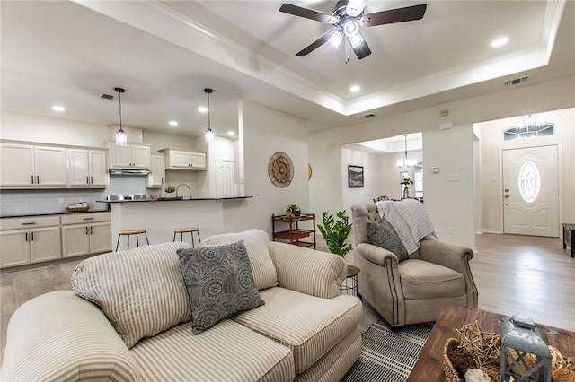 living room featuring ornamental molding, ceiling fan with notable chandelier, light hardwood / wood-style flooring, and a tray ceiling