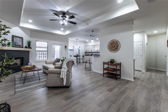 living room with crown molding, a raised ceiling, hardwood / wood-style flooring, ceiling fan, and a fireplace