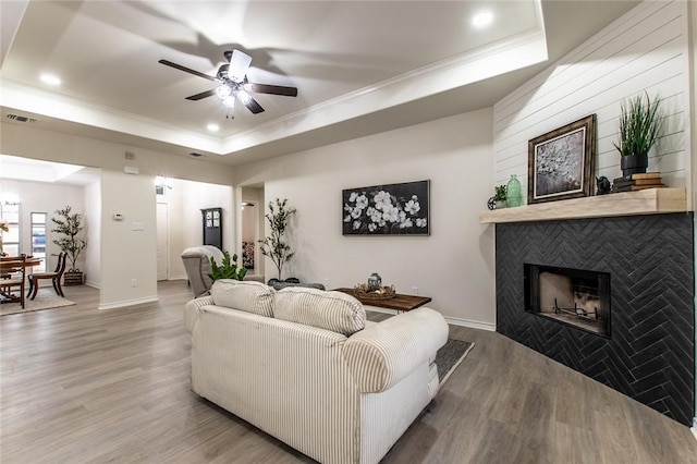 living room with a raised ceiling, wood-type flooring, ceiling fan, and a fireplace