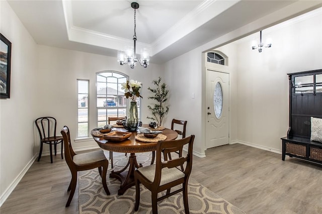 dining area with an inviting chandelier, ornamental molding, a raised ceiling, and light wood-type flooring