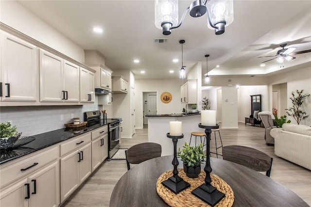 kitchen featuring decorative light fixtures, a breakfast bar area, decorative backsplash, light hardwood / wood-style floors, and electric stove