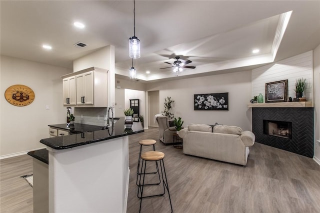 kitchen featuring light hardwood / wood-style flooring, white cabinetry, a kitchen bar, decorative light fixtures, and a raised ceiling