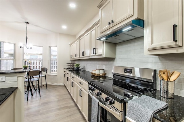 kitchen featuring stainless steel electric range oven, decorative light fixtures, light hardwood / wood-style flooring, dark stone countertops, and decorative backsplash