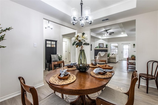 dining space featuring ceiling fan with notable chandelier, light wood-type flooring, and a tray ceiling