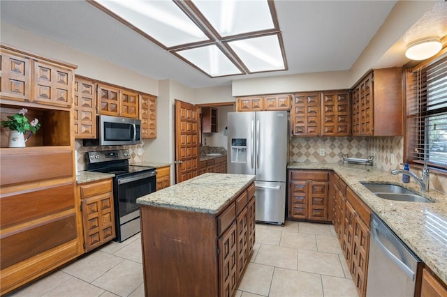 kitchen with sink, appliances with stainless steel finishes, a center island, light stone counters, and light tile patterned flooring